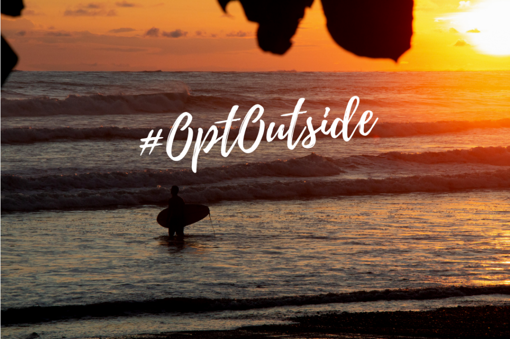 Surfer in the ocean at sunset with text #OptOutside