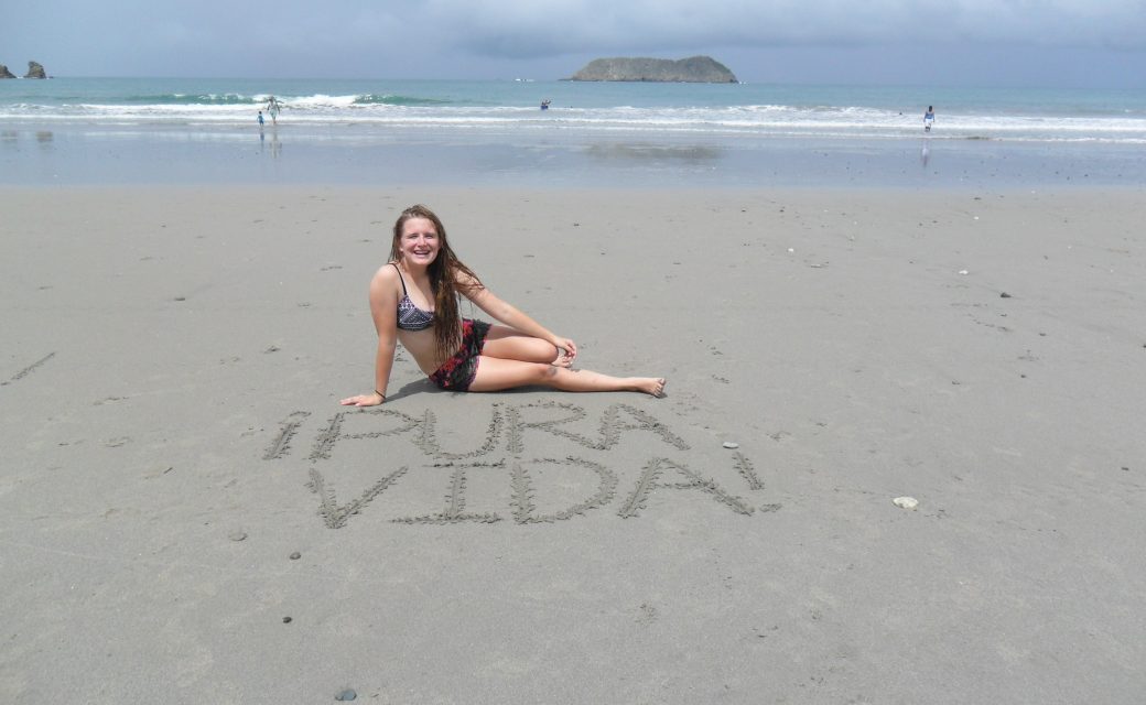 A girl lay on the beach with pura vida written in the sand