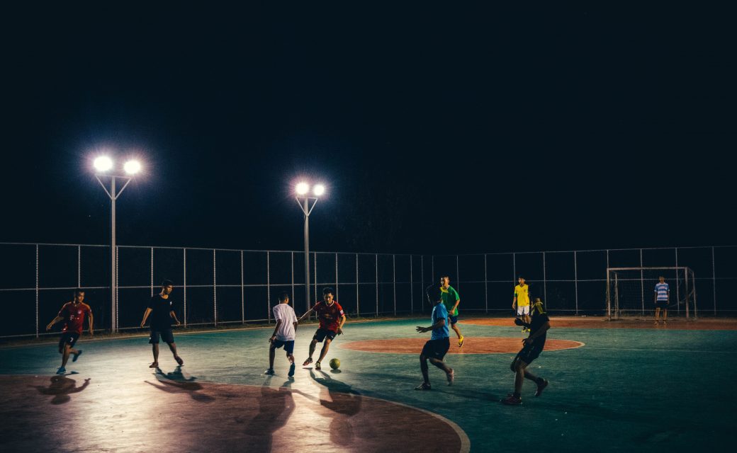 A group of men playing a futsal game with floodlights