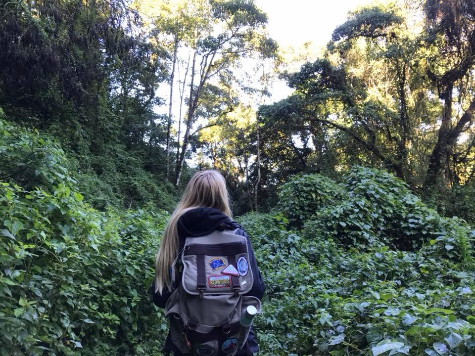 A girl with long blonde hair and a backpack walking through the jungle